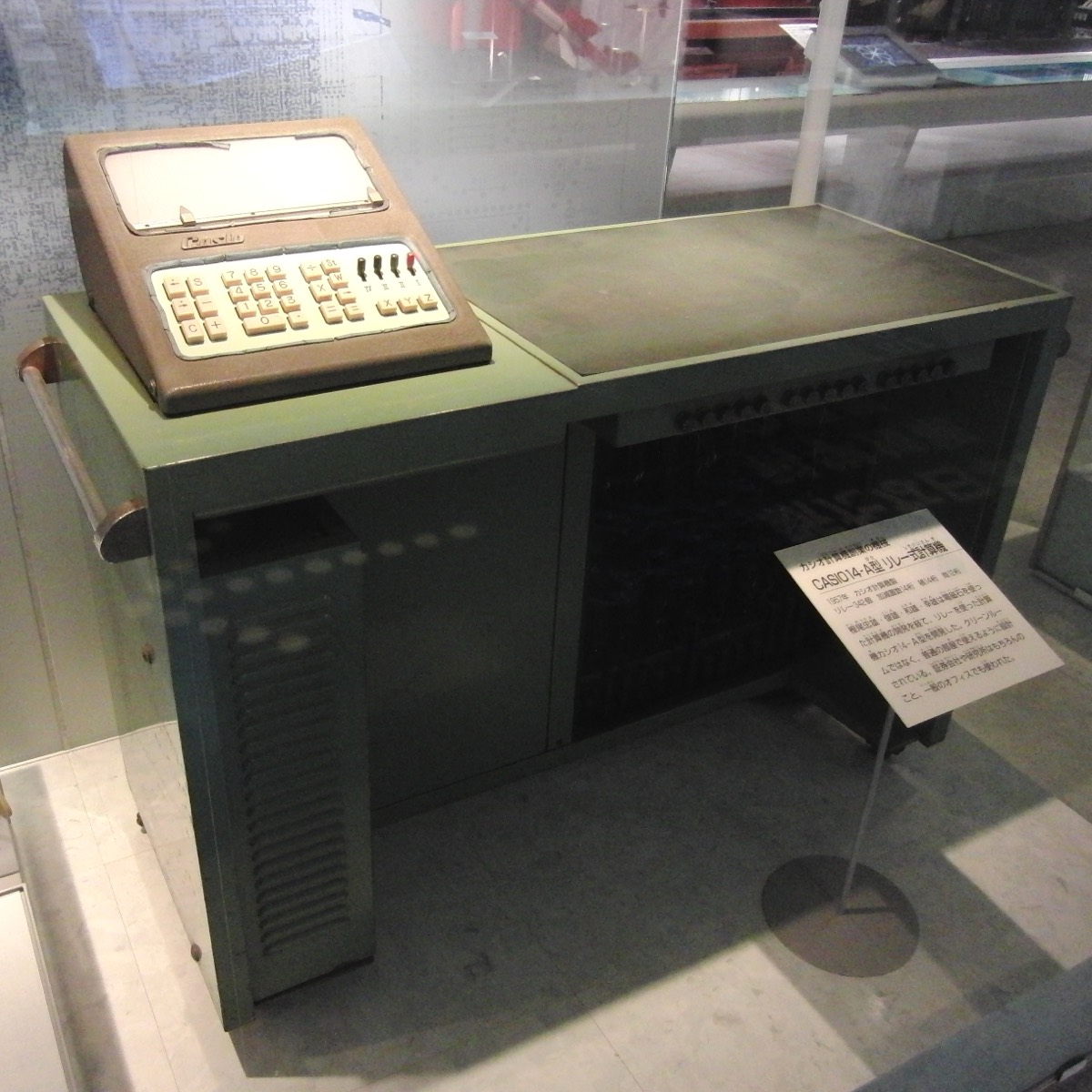 The 1957 Casio 14-A calculator, the size of an office desk, inside a display case at the National Museum of Nature and Science in Tokyo. On top, a brown console with a keyboard and the Casio name.